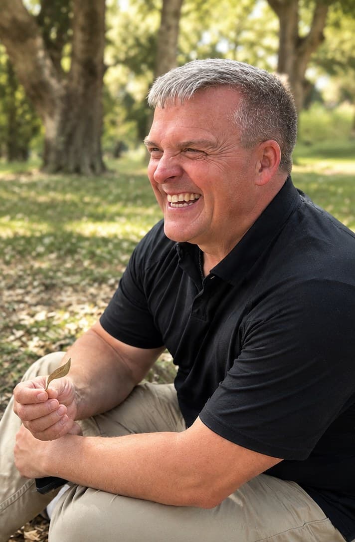 Robert Upton laughing while sitting outdoors under the trees